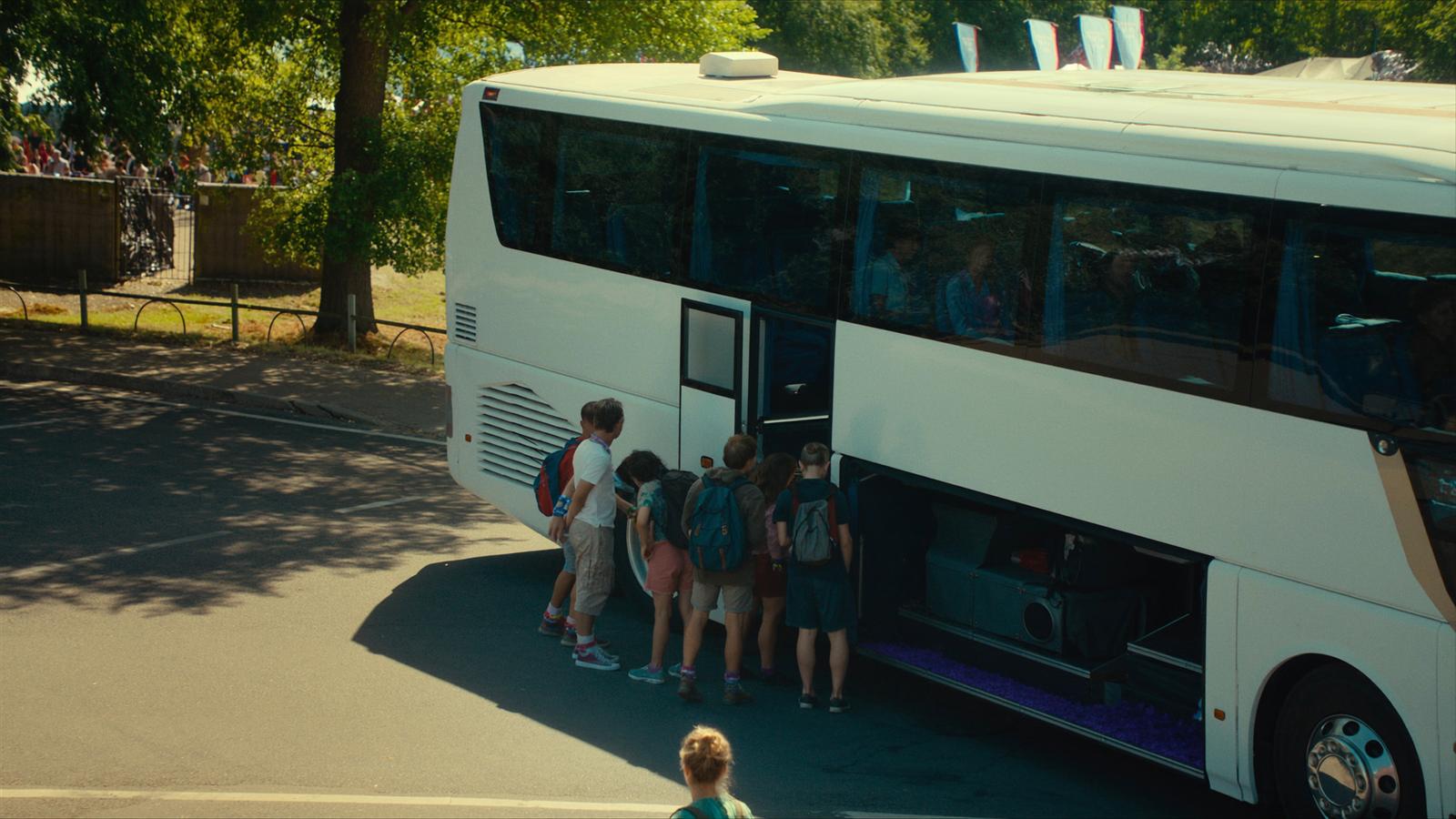 Autocar de luxe moderne garé sur le site d'un festival de musique en Belgique, jeunes festivaliers montant à bord avec leurs sacs à dos, lumière dorée de fin d'après-midi